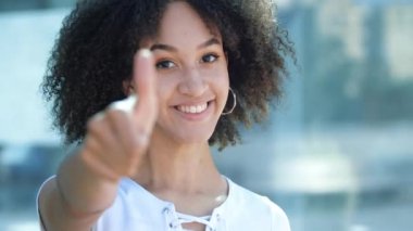 Afro saçlı, dişlek gülümseyen mutlu Afro-Amerikalı kız, baş parmağını kaldırıyor, iyi niyet ve onaylama jesti, iyi kalite. Pozitif duygular vücut dili Güzel genç bir kadın evet dedi. 