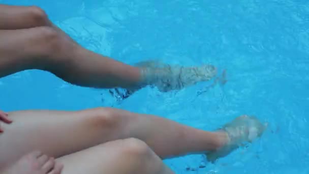 Dos descalzos bronceado joven modelo sentado junto a la piscina alegría luz del sol pruebas de agua azul patadas pie tembloroso en la piscina pública hacer hermosas salpicaduras grandes olas en el descanso exótico viaje turístico, vista de cerca — Vídeo de stock