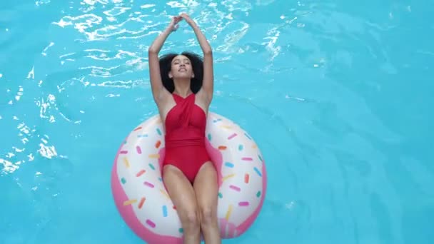 Etnické kudrnaté ženy vznášející se v modré vodě v hotelovém bazénu v nafukovací trubici zvednou ruce nad hlavu a usmějí se na kameru. Afro student dívka relaxovat v turistickém komplexu plavání na kruhu — Stock video