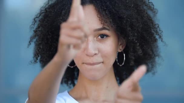 Γοητευτικό κομψό African American έφηβος κορίτσι με afro χτένισμα κάνει πιστόλια χέρι χτύπησε γκολ, προσποιείται να πυροβολήσει όπλο από τα δάχτυλα χαμόγελο ευτυχώς toothy. Όμορφη νεαρή γυναίκα φλερτάρει διασκεδαστικά με αυτοπεποίθηση — Αρχείο Βίντεο