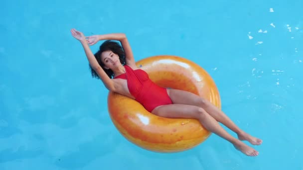 年轻而快乐的黑发女子，红发苍苍，举手表决，自由自在，闭上双眼，坐在橙色的橡胶圈里，在国内热带酒店度假胜地的游泳池里游泳 — 图库视频影像