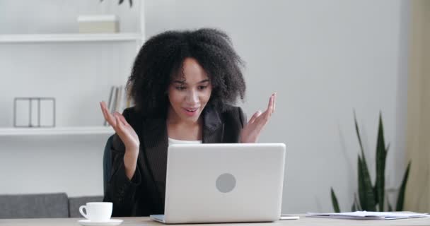 Succesvolle Afrikaanse jonge vrouw zit aan tafel maakt gebruik van laptop lees e-mails online thuiskantoor, krijgt goed nieuws, positieve examenresultaten, nieuwe kans, voelt vreugde triomphe, viert overwinning, gelukkig dansen — Stockvideo