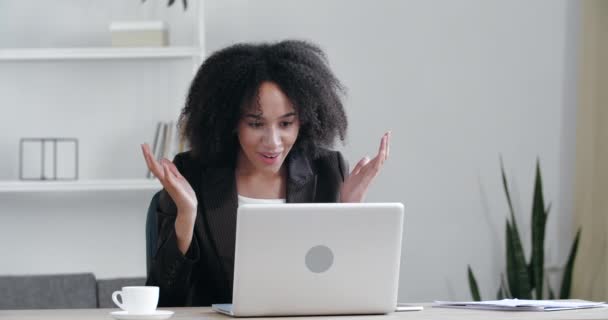 Erfolgreiche junge Afrikanerin sitzt mit Laptop am Tisch, liest E-Mails online im Home Office, bekommt gute Nachrichten, positive Prüfungsergebnisse, neue Chancen, fühlt Freude, feiert Sieg, fröhliches Tanzen — Stockvideo