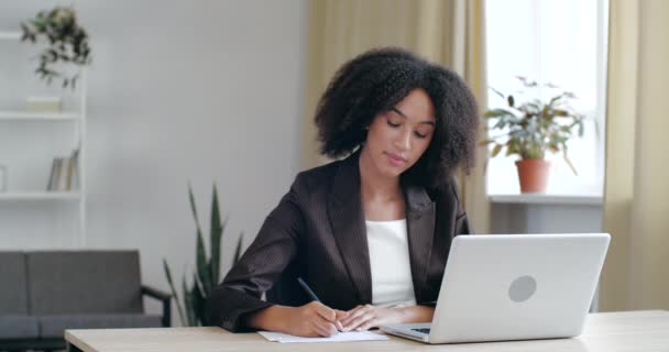 Asesor financiero profesional africano milenario enfocado que mantiene servicios de soporte de videollamadas con el cliente. Estudiante estadounidense joven concentrado motivado que estudia en cursos en línea, escribiendo notas — Vídeo de stock