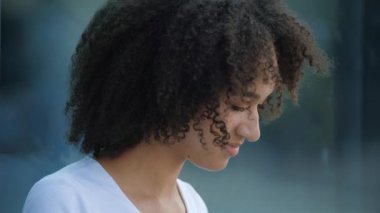 Güzel afro-amerikan gülümseyen genç kadın dışarıda dizüstü bilgisayarla yazmayı seviyor. Panoramik pencerenin kenarında oturuyor. Modern binanın yansıtıcı penceresi, yakın görüş, yavaş çekim.