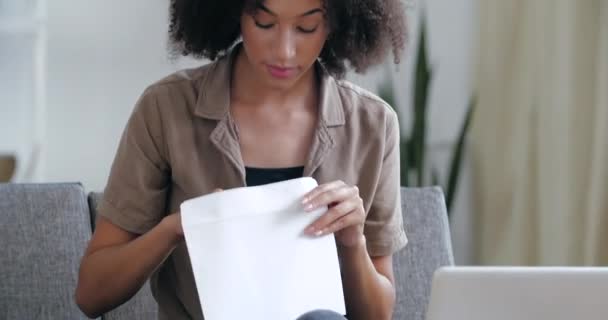 Retrato feliz sorprendido afroamericano dama ganadora cheque correspondencia sentir victoria contento recibir leer buenas noticias en papel factura correo electrónico carta entusiasmado con el impuesto de aprobación de préstamos bancarios sentarse en el sofá en casa — Vídeos de Stock