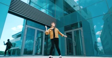 Genç öğrenci mutlu ve rahat hissediyor, zaferi kutlamak için dans ediyor. Sokakta egzersiz yapan genç dansçı, vücudun müzik için ritmik eğitimi, aktif hareketler, sokak dansı