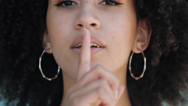 彼女の唇と口に彼女の人差し指を入れて、アフロと深刻な顔を持つ美しい少女のクローズアップ肖像画。アフリカ系アメリカ人の女性は、静かで静かなジェスチャーを求めています。秘密を守りプライバシーを守る. — ストック動画