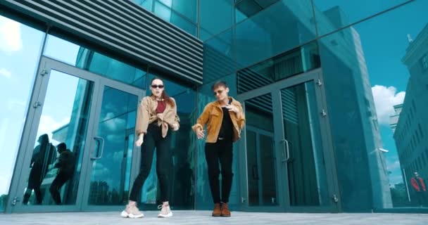 Dos estudiantes pasan tiempo libre al aire libre, se divierten en el clima soleado. Una chica y un chico joven con ropa elegante bailando con música moderna. Ensayando coreografía danza street hip-hop danza contemporánea — Vídeos de Stock