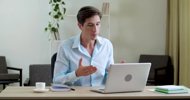 Зайнятий серйозний чоловік сидить в офісній домашній кімнаті за столом з ноутбуком, використовує веб-камеру для переговорів, виступає на відеоконференції, спілкується по телефону в Інтернеті, проводить інтерв'ю дистанційно в карантині — стокове відео