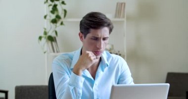 Düşünceli, odaklanmış çekici bir adam ev masasında çalışıyor, dizüstü bilgisayarda yazı yazıyor, sorunları internetten çözüyor, internette bilgi arıyor, düşünüyor, kararlarını veriyor, çenesini düşünceye daldırıyor.