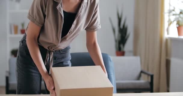 Junge Hausfrau Afroamerikanerin betritt Zimmer, trägt Päckchen von der Post, Karton mit Bestellung, packt Geschenkartikel aus Internet-Shop aus, blickt interessiert, freut sich über Kauf, Nahaufnahme — Stockvideo