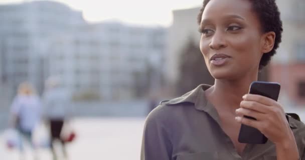 Active African American woman dances on street, moves rhythmically to music from smartphone, listens online radio on network, sings song in telephone like microphone, carefree lifestyle enjoying youth — Stock Video