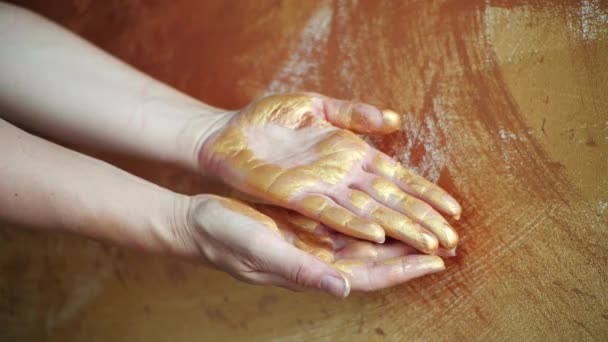 Una joven pinta lentamente en el aire, muestra la palma abierta con las manos en un estudio de arte. Pintura dorada brillante en las palmas de los artistas. Hermosos movimientos de mano lentos y elegantes son como la danza. — Vídeos de Stock