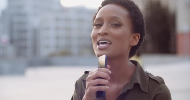 Portret van een gelukkige Amerikaanse vrouw die een lied zingt in telefoon als in een microfoon. Afrikaanse etnische dame in casual korte haren jurk glimlachen dansen op muziek in de straat, een persoon partij, stedelijke scène, close-up — Stockvideo
