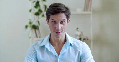 Genç, komik bir adamın portresi, apartman dairesinde oturuyor, kameraya duygusal bir yüz ifadesiyle bakıyor, başını ritimli bir şekilde yana hareket ettiriyor, kaşlarıyla oynuyor, şımartıyor, flört ediyor, yakın plan çekiyor.