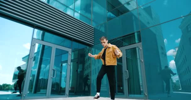 Šťastný radostný mladý evropský tisíciletý muž dospívající těší pohyblivé nohy, mává pažemi tančícími ve vzduchu, třesoucí se rukou zábavu na pozadí moderní městské budovy, atraktivní mužský model aktivně pózuje — Stock video