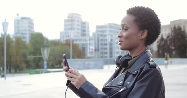 时尚的混合种族博客女孩站在城市里，手里拿着手机，用智能手机与朋友交流，在网上聊天，接听视频电话，在网上开会 — 图库视频影像