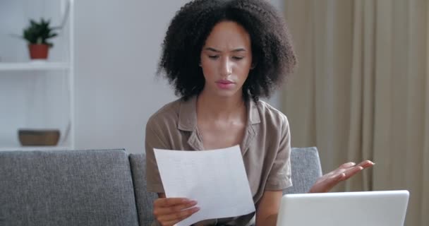 Joven mujer africana extranjera sentada en el sofá chequeando el correo, recibiendo carta de desalojo, aviso de deuda del arrendatario, sintiéndose molesto miedo desesperado, preocupado, esperanzas de solución, concepto de problema — Vídeos de Stock