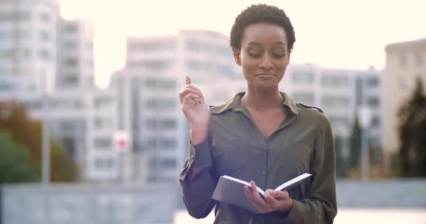 Femme africaine drôle se tient dans la rue, réfléchit, se souvient de l'information, obtient idée de concept, écrit des connaissances dans le carnet, assez pouces levés. BD visage féminin de dame ethnique prise de décision — Video