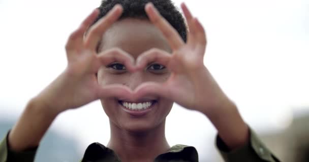 アフリカの美しい笑顔の白い歯の女性の頭のショットは、彼女の前に彼女の手を置き、心の形で彼女の指を折る、親しみやすさのサイン、愛のシンボルサポート優しさ、ロマンチックなジェスチャー — ストック動画