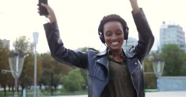 Kulaklık takan, siyah deri ceket giyen, elinde akıllı telefon tutan, müzik dinleyen şehir sokaklarında dans eden Etnik Amerikalı bir kız. Genç melez kadınlar zıplamaktan ve el sallamaktan hoşlanır.