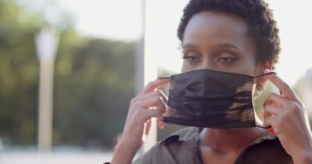 Porträtt av isolerad etnisk flicka stående på gatan sätta på svart medicinsk mask på kvinnligt afrikanskt ansikte, skydda sig från covid virus, pandemisk tid, pollen allergi säsongssjukdom, närbild — Stockvideo