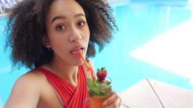 Afrikalı etnik kadın vlogger, bilardo kompleksinde blog için canlı yayın yapıyor, kamerada alkolsüz mojito kokteyli içiyor, selfie için poz veriyor, video konferansı için akıllı telefon kullanıyor.