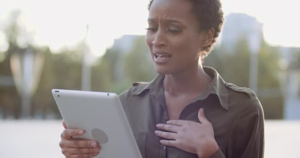 Gros plan de femme afro-américaine bouleversée utilisant une tablette informatique pour discuter en ligne en vidéoconférence à l'extérieur. Portrait de fille ethnique malheureuse, sentiment de chagrin, visage triste, concept d'échec du problème — Video