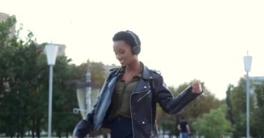 Etkin etnik genç kız şık giyiniyor, kulaklık takıyor, müzik dinliyor, kadın vücuduyla dans ediyor, aktif olarak seslere yöneliyor, şarkı söylüyor, akıllı telefonlardan melodik müzik dinliyor.