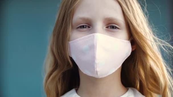 Közelkép a női gyermek arcáról orvosi rózsaszín maszkban, védelem a corona vírussal szemben, vissza az iskolába influenza világjárvány idején, fertőzés kockázata. Egy iskolás lány portréja, aki komolyan nézi a kamerát. — Stock videók