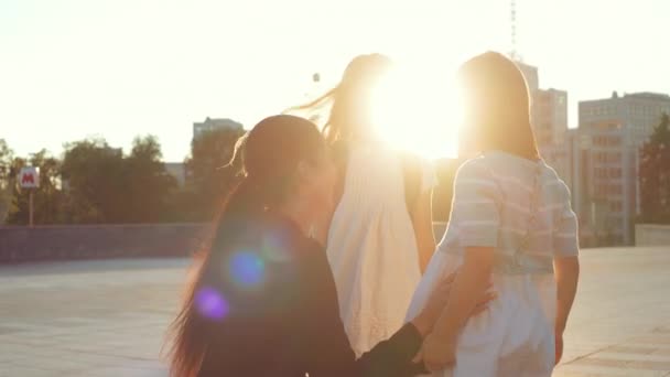 Close up good looking brunette mum woman parent embracing two little kid sisters pupil on schoolyard. Mother talking smiling pretty daughters, sends off school girls with backpacks on sunset outdoor — Stock Video