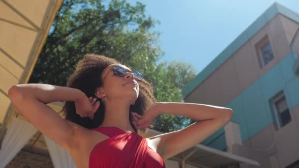 时尚迷人的非洲裔美国女人，穿着比基尼摆出姿势，直着头发，在夕阳西下的背景下漫步在休息室餐厅的后院，在温泉度假 — 图库视频影像