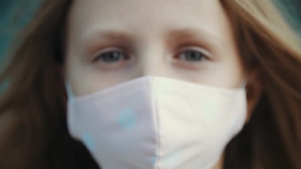 Primo piano del volto della bambina in maschera rosa medica, protezione dal virus della corona, ritorno a scuola durante la pandemia influenzale, rischio di infezione. Ritratto di studentessa che guarda seriamente la macchina fotografica — Video Stock