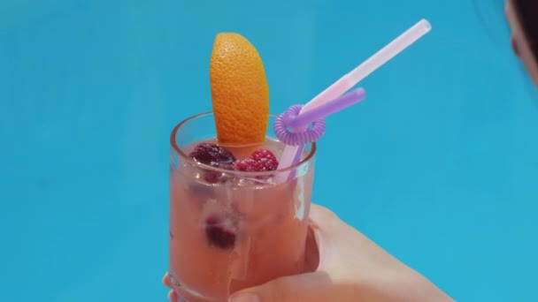 Une main bronzée femelle tient un verre froid de cocktail de boissons saines non alcoolisées et fruitées avec de la paille, apporte de la limonade à sa bouche et jouit d'un goût rafraîchissant lors d'une journée chaude, vue rapprochée — Video