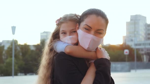 작은 딸이 호흡기 바이러스 감염으로부터 보호 해 주는 마스크를 쓰고 있는 갈색의 코카서스 엄마. 질병의 위험, 세계적 인 개념. 해가 지면 엄마를 껴안고 있는 소녀 — 비디오