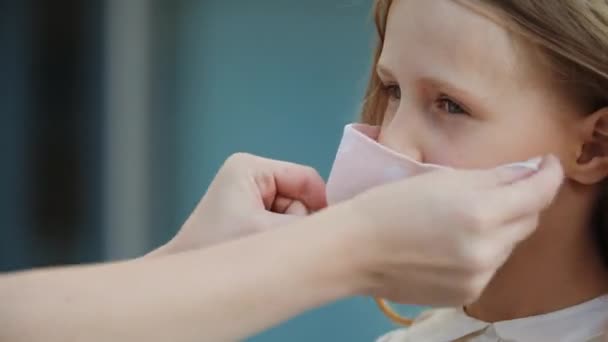 Close up of female hands put medical mask on face of little cute girl, protect from virus, take care of health of child outdoors, modern family life in pandemic epidemic of respiratory disease — Stock Video