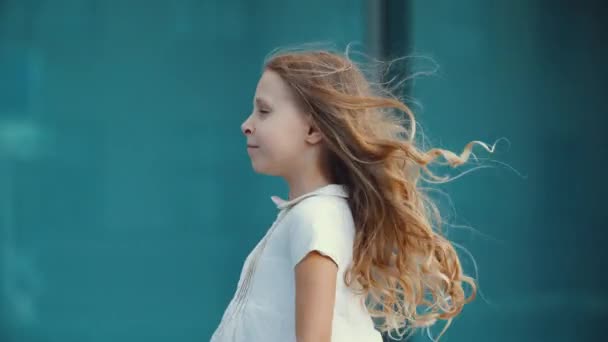 Κοντινό πλάνο του μοναχικού μικρού κοριτσιού, ξανθιά κόρη σε λευκό φόρεμα, στέκεται ποζάροντας μπροστά από την κάμερα, χορεύει παιδιά, ενεργά χαρούμενες κινήσεις, κουνάει το σώμα της προς τα πλάγια, ο άνεμος αναπτύσσει μακριά χρυσά μαλλιά — Αρχείο Βίντεο