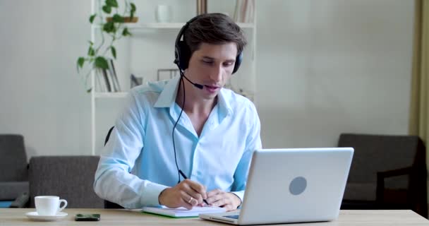 Φιλικός επιχειρηματίας φορούν ασύρματα ακουστικά κάθεται στο γραφείο, κάνοντας τηλεδιάσκεψη βιντεοκλήση στο laptop web cam. Χαμογελώντας αρσενικό διευθυντή τηλεφωνικού κέντρου πράκτορα, έχοντας σε απευθείας σύνδεση συνομιλία δίκτυο απόστασης συνέντευξη εργασίας — Αρχείο Βίντεο