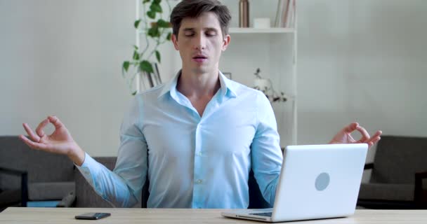 Focalisé jeune homme d'affaires pratique le yoga en méditant dans le bureau à la maison après un travail acharné. Calmer le stress masculin, prendre une pause assis au bureau, faire un exercice de respiration profonde asana, concentré d'harmonie — Video