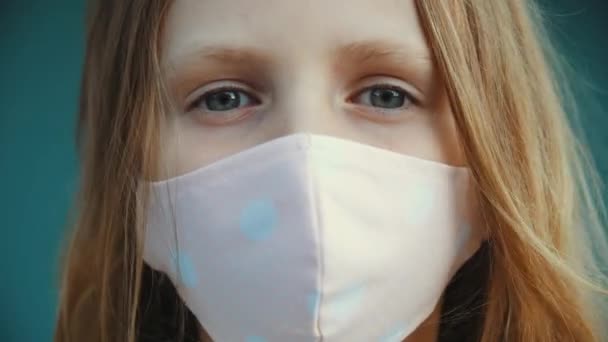 어린 소녀의 모습이 카메라에 비춰져 있고, 아이가 감염성 고질적 인 바이러스로부터 보호 해 주는 의료용 마스크를 얼굴에 쓰고 있고, 작은 숙녀가 질병이 창궐하는 동안 거리에 서 있습니다. — 비디오