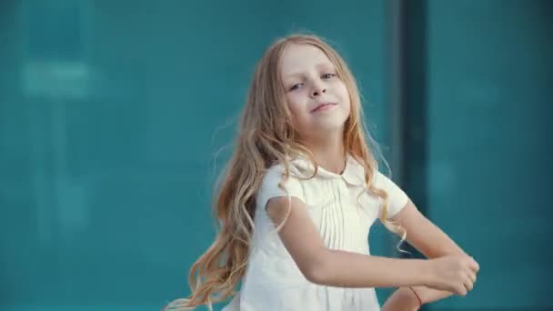 Κοντινό πλάνο του ενεργού κοριτσιού θηλυκό παιδί με χρυσά μαλλιά, φορώντας λευκό κομψό φόρεμα, χορό στο δρόμο, κινείται χαρούμενα, κουνώντας τα χέρια της σε διαφορετικές κατευθύνσεις, εκτελεί την κίνηση στην κάμερα — Αρχείο Βίντεο