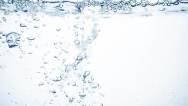 Μεγάλη γυαλιστερή σταγόνα νερού σε αργή κίνηση πέφτει στην λεία καθαρή επιφάνεια, δημιουργώντας φυσαλίδες αέρα, πιτσιλιές και κυματισμούς μετά την πτώση σε, πλευρική άποψη. Φρεσκάδα του κυανού υγρού σε λευκό φόντο — Αρχείο Βίντεο