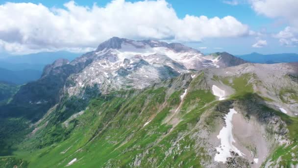 Vista aérea de Oshten pico de natureza majestosa deslumbrante do Cáucaso para Mountain Fisht, coberto com pedras de neve e grama sob nuvens brancas no céu azul. Sunglare sunraise in summer, Adygea, Rússia — Vídeo de Stock