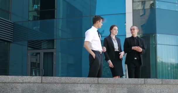 Trzech młodych pracowników stojących w pobliżu centrum biznesowego w przerwie od pracy, aktywnie żartujących, koncepcja przyjacielskich kolegów. Dwóch młodych mężczyzn i kobieta w klasycznych garniturach omawiają wiadomości na świeżym powietrzu — Wideo stockowe