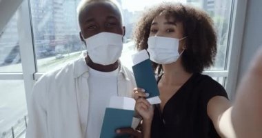 Yabancı Afro-Amerikalı gençler ellerinde pasaportlarıyla bir arada duruyorlar, webcam 'de uçak biletlerini gösteriyorlar, görüntülü sohbet yapıyorlar, virüse karşı koruyucu maske takıyorlar.