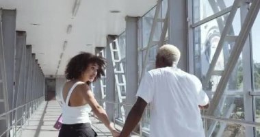 Genç Afrikalı kız ve Amerikalı erkek birlikte alışverişe gidiyorlar, ellerinde alışveriş hediyeleri olan parlak kağıt torbaları taşıyorlar, tatmin olmuş müşteriler indirimli ürünler alıyorlar, Kara Cuma konsepti.