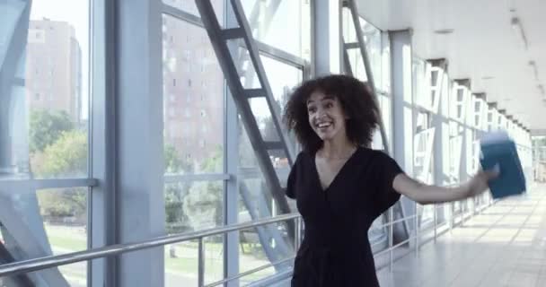 Mixed race curly haired young attractive woman walks in lobby of terminal with suitcase, waves to her husband, greets boyfriend. African man meets wife or sister at airport, tight hugs of two people — Stock Video