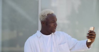 Beyaz elbiseli genç Afrikalı Amerikalı hippi sokakta tek başına duruyor, cep telefonunu elinde tutuyor, internet üzerinden webcam konferansına, modern teknoloji kavramına hitap ediyor.