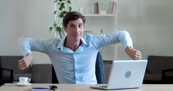 Активный веселый молодой бизнес-менеджер делает упражнения в офисе сидя за столом, активно двигая руками, крутя руками, танцуя на работе во время перерыва, занимаясь гимнастикой для мужского тела — стоковое видео